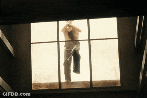A Man Without A Shirt Is Standing In A Window GIF