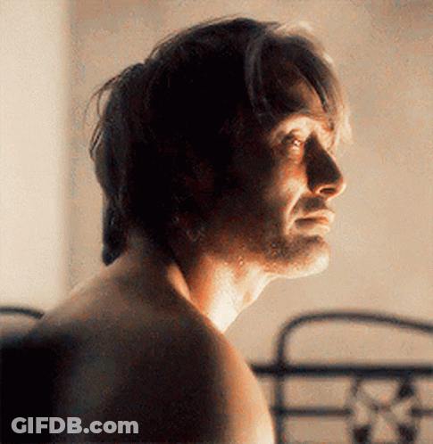A Man Without A Shirt Is Standing In Front Of A Bed Looking At The Camera . GIF