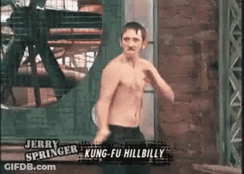 A Man Without A Shirt Is Standing In Front Of A Brick Wall In A Room . GIF