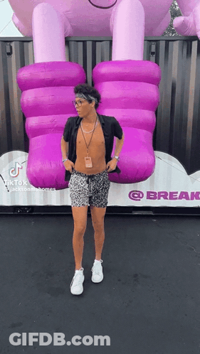 A Man Without A Shirt Is Standing In Front Of A Giant Inflatable Purple Elephant . GIF