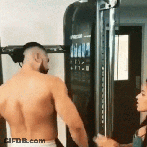 A Man Without A Shirt Is Standing In Front Of A Machine In A Gym . GIF