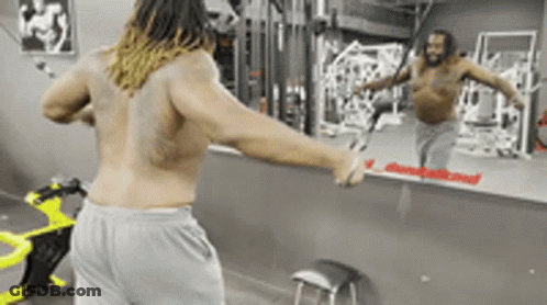 A Man Without A Shirt Is Standing In Front Of A Mirror In A Gym GIF