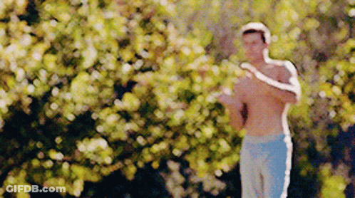 A Man Without A Shirt Is Standing In Front Of A Tree . GIF