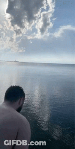 A Man Without A Shirt Is Standing In The Water Looking At The Ocean GIF