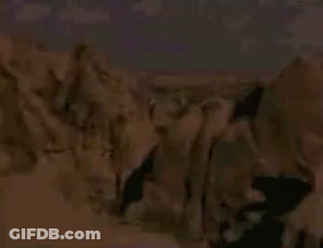 A Man Without A Shirt Is Standing Next To A Large Rock . GIF