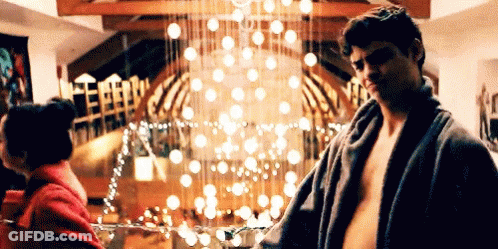A Man Without A Shirt Is Standing Next To A Woman In A Room With A Christmas Tree In The Background . GIF