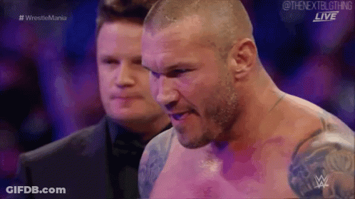 A Man Without A Shirt Is Standing Next To Another Man In A Wrestling Match . GIF