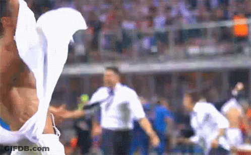 A Man Without A Shirt Is Standing On A Soccer Field With A White Shirt On GIF