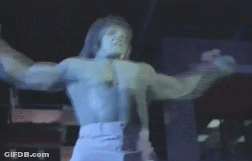 A Man Without A Shirt Is Standing On A Stage With His Arms Outstretched And Singing Into A Microphone . GIF