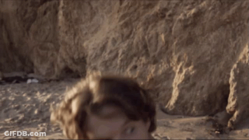 A Man Without A Shirt Is Standing On The Beach Looking At The Camera GIF