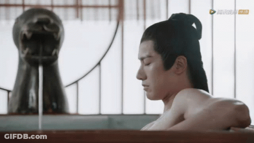 A Man Without A Shirt Is Taking A Bath In A Bathtub In Front Of A Statue Of A Dragon GIF