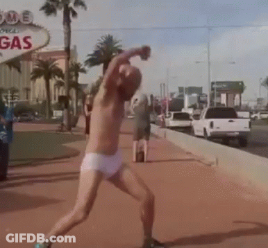 A Man Without A Shirt Is Throwing A Ball In Front Of A Sign That Says Gas GIF
