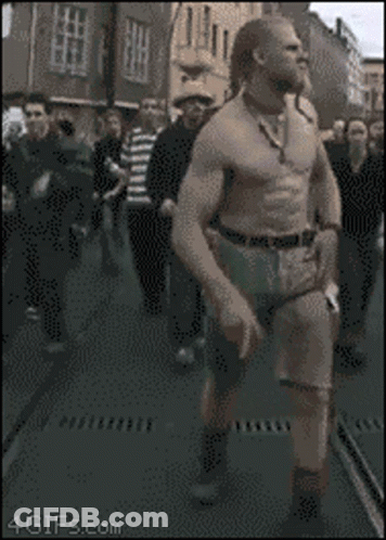 A Man Without A Shirt Is Walking Down A Street In Front Of A Crowd Of People With The Website 4Gifs.com Visible GIF