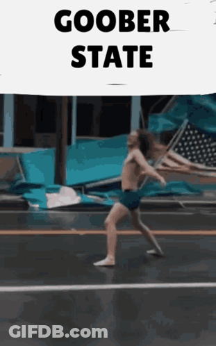 A Man Without A Shirt Is Walking Down A Street With A Sign That Says Goober State GIF