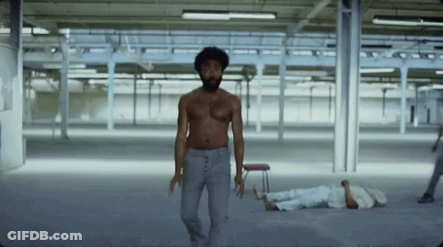 A Man Without A Shirt Is Walking In An Empty Room While A Man Laying On The Floor . GIF