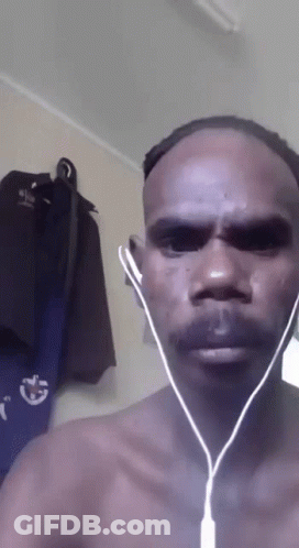 A Man Without A Shirt Is Wearing Ear Buds In Front Of A Wall With Clothes Hanging GIF