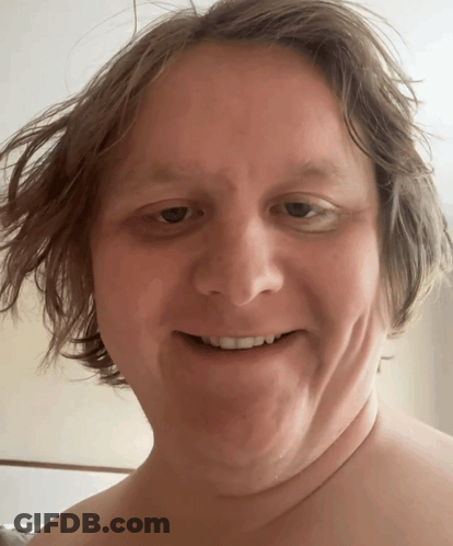 A Man Without A Shirt Smiles For The Camera GIF