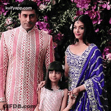A Man , Woman , And Child Are Posing For A Picture In Front Of Flowers . GIF