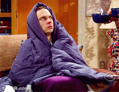 A Man Wrapped In A Purple Blanket Sits On A Couch GIF