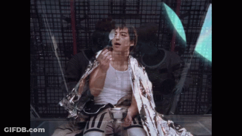 A Man Wrapped In A Silver Blanket Holds A Cup GIF