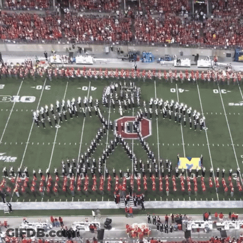 A Marching Band Is Performing On A Football Field With The Letter M On The Field GIF
