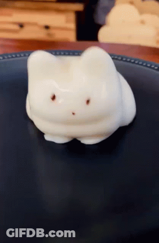 A Marshmallow In The Shape Of A Cat Laying On A Black Plate GIF