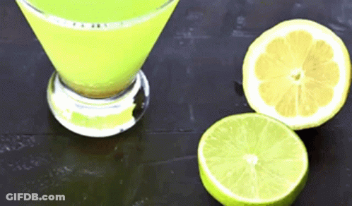 A Martini Glass Filled With A Yellow Liquid Next To Two Sliced Limes GIF