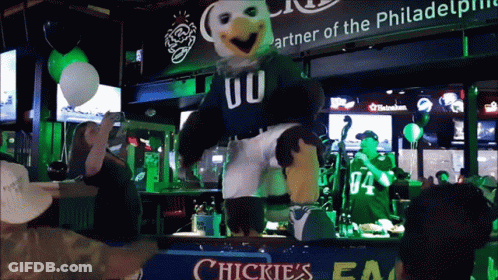 A Mascot Dancing In Front Of A Sign That Says Chickies GIF