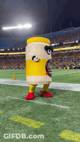 A Mascot Dressed As A Jar Of Mustard Is Standing On A Football Field . GIF