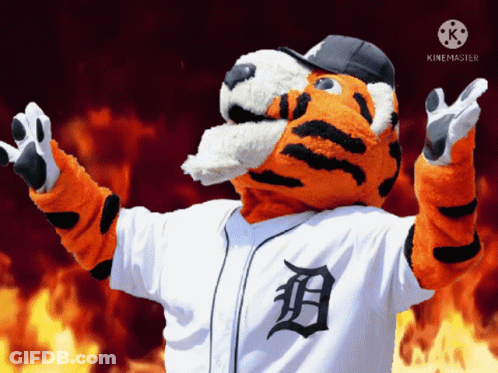 A Mascot For The Detroit Tigers Stands In Front Of A Fire Background GIF