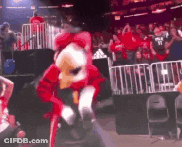 A Mascot In A Red And White Costume Is Dancing In Front Of A Crowd . GIF