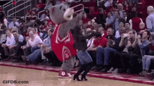 A Mascot Is Dancing On A Basketball Court With A Crowd Watching . GIF