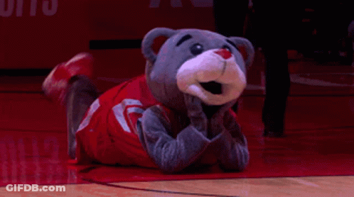 A Mascot Is Laying On A Basketball Court With His Hands Folded GIF