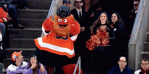 A Mascot Is Standing In The Stands With A Cheerleader In Front Of Him GIF