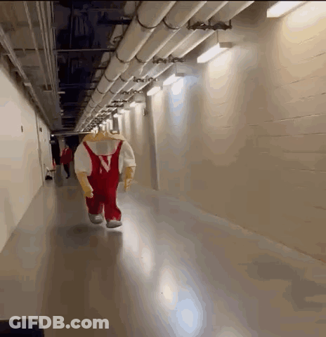 A Mascot Is Walking Down A Hallway With Pipes GIF