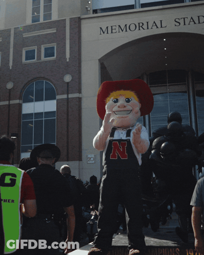 A Mascot Standing In Front Of A Building That Says Memorial Stadium GIF