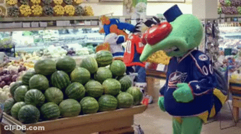A Mascot Standing In Front Of A Display Of Watermelons GIF