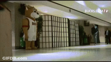 A Mascot Wearing A Bucks Jersey Is Standing In A Hallway .. GIF