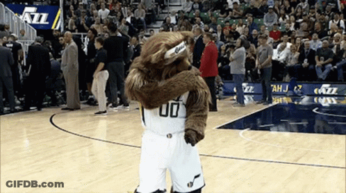 A Mascot Wearing A Number 00 Jersey Is Hugging Another Mascot On A Basketball Court GIF