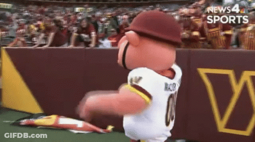 A Mascot Wearing A Redskins Jersey Is Dancing On A Field GIF
