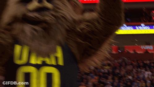 A Mascot Wearing A Utah Jersey Stands In Front Of A Crowd At A Basketball Game GIF