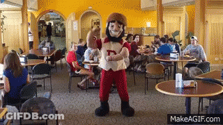 A Mascot With The Letter D On His Shirt Stands In A Restaurant GIF