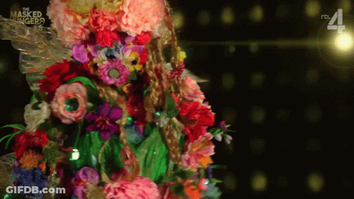 A Masked Singer Costume With Flowers And Leaves On It GIF