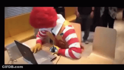 A Mcdonald 'S Clown Is Sitting At A Table Using A Laptop Computer GIF