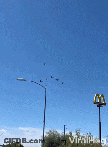 A Mcdonald 'S Sign Is In The Foreground Of A Group Of Planes In The Sky GIF