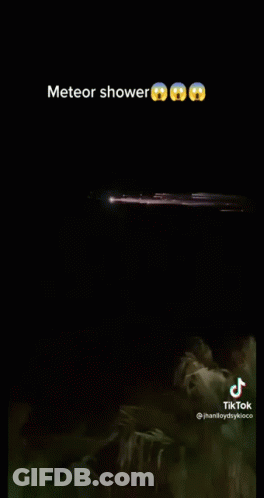 A Meteor Shower Is Visible In The Night Sky Over A Body Of Water . GIF