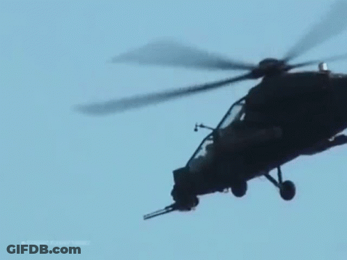 A Military Helicopter Is Flying In A Blue Sky . GIF