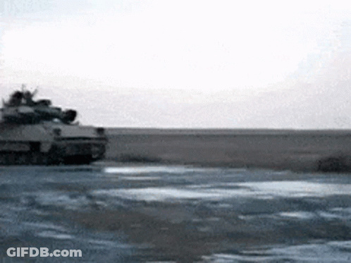 A Military Tank Is Driving Down A Dirt Road GIF