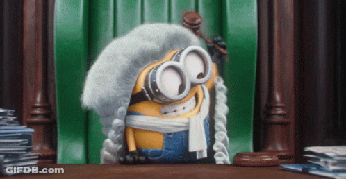 A Minion Wearing A Wig And Goggles Is Holding A Gavel In Front Of A Green Curtain GIF