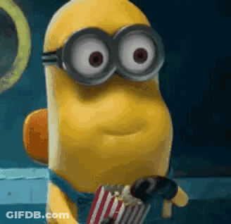 A Minion Wearing Goggles Is Holding A Bag Of Popcorn And A Chocolate Bar . GIF